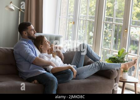Couple in love relaxing on couch daydreaming looking out window Stock Photo