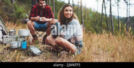 Cheerful young couple having some coffee while camping in nature. Happy young couple having a good time on a camping holiday. Stock Photo