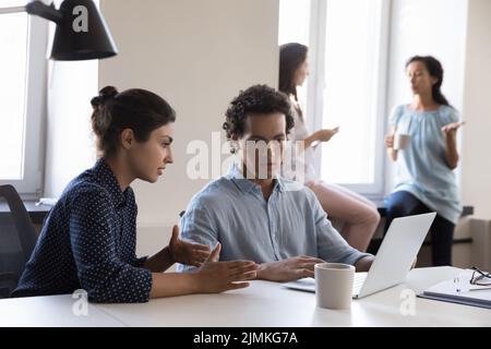 Multiracial colleagues talking sit at desk in office with laptop Stock Photo