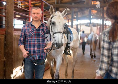 Couple of farmers with bucket before horse standing at stabling Stock Photo