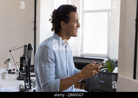 Smiling successful Hispanic businessman using smartphone at workplace Stock Photo