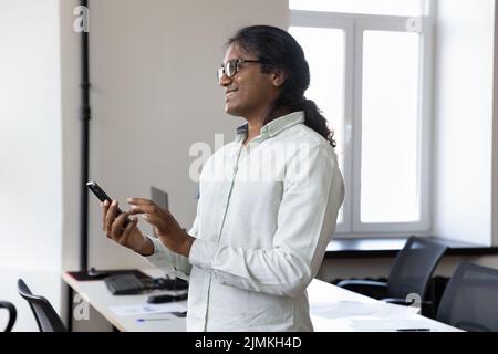 Thoughtful Indian man entrepreneur standing in office with smartphone Stock Photo