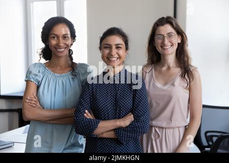 Three multiethnic businesswomen pose at workplace smile staring at camera Stock Photo