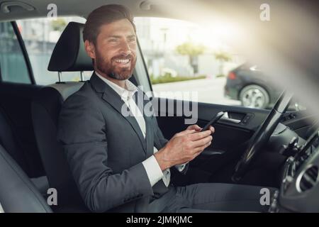 Smiling businessman in grey suit is riding behind steering wheel of car and using phone Stock Photo