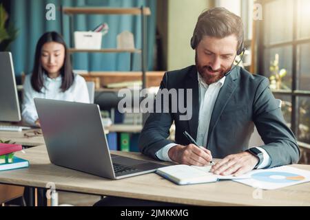 Male operator using headset and computer while talking with customers online on colleague background Stock Photo
