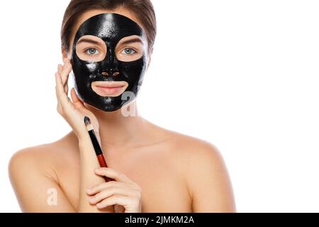 Beautiful woman is applying purifying black mask on her face Stock Photo