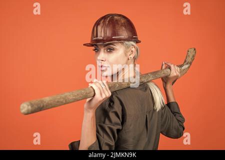woman architect in protective helmet and boilersuit hold shovel on orange background, building Stock Photo