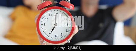 Red alarm clock against the background of a sleeping couple Stock Photo