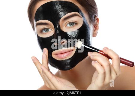 Beautiful woman is applying purifying black mask on her face Stock Photo