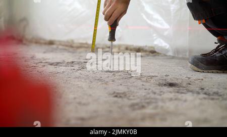 Installation of beacons on the floor. A worker drives a screw into the floor. Floor renovation concept. A worker's hand with a screwdriver is screwing Stock Photo