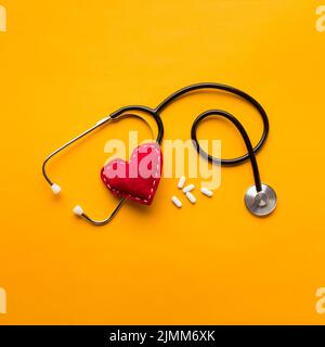 High angle view stethoscope stitched heart medicines yellow backdrop Stock Photo