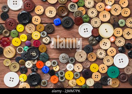 Many colorful buttons brown thread needle wooden background Stock Photo