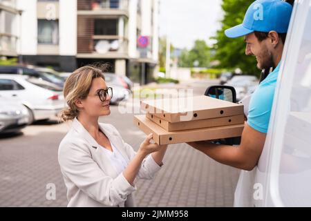 Delivery man in a white van delivers pizza to a woman client Stock Photo