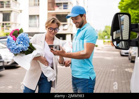 Young delivery man in blue uniform delivers flowers to a woman client Stock Photo