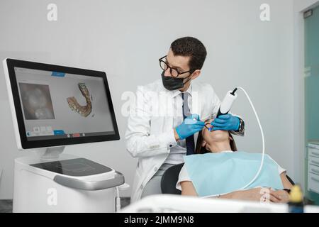 Male orthodontist scaning patient with dental intraoral scanner and controls process on screen. Prosthodontics and stomatology concept. Stock Photo