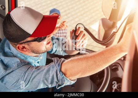 Caucasian Trucker in His 30s Sitting in the Cab of His Truck Tuning the Citizens Band Radio with Help of His Colleague. Preparations Before Starting t Stock Photo