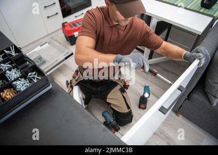 Caucasian Male Worker Installing the Handle to the Kitchen Cabinet Door Using Screwdriver. Modern New Kitchen and Other Professional Tools for Install Stock Photo