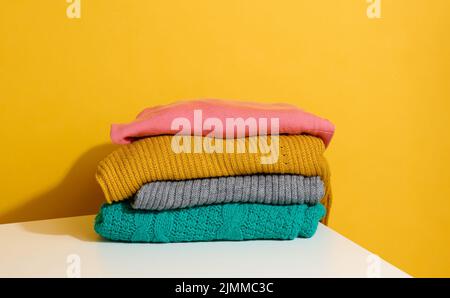 Stack of folded knitted sweaters on yellow background. Comfortable clothes, wash Stock Photo
