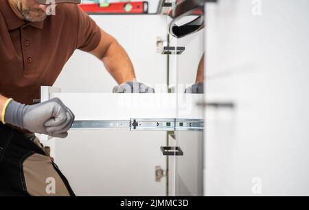 Caucasian Household Worker Assembling Drawer Slide Element to Install Roll-Out Shelf in the Cabinet. Kitchen Renovation and Furnishing Theme. Stock Photo