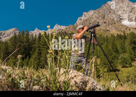 Traveling Nature Photographer Standing in the Middle of Scenic Landscape Taking a Photo of the Alpine Mountains With His Camera Mounted on a Tripod. Stock Photo