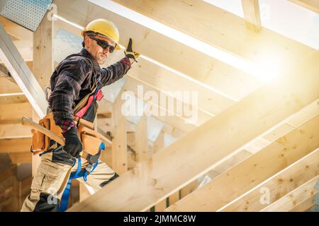 Fully Equipped Professional Construction Worker Securing Wooden Planks in the Roof Section Skeleton of New Residential House Hammering Nails With a Ha Stock Photo