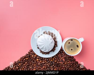 White cup with hot coffee, coffee beans and marshmallows on a pink background. Stock Photo