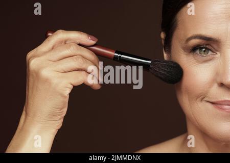 Middle aged woman applying foundation powder or blush on her face Stock Photo