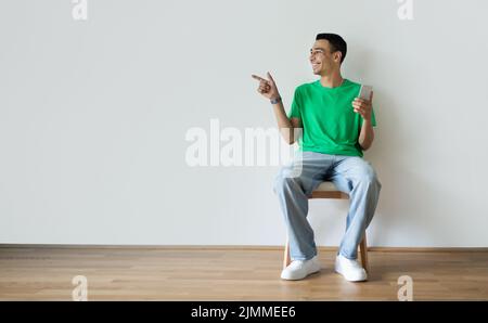 People and technology concept. Young arab man holding cellphone and pointing finger aside at copy space Stock Photo