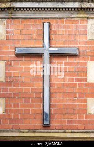 Shiny metal cross mounted on red brick wall of modern church. Stock Photo
