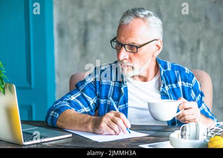 Senior man looking laptop holding pen making notes Stock Photo