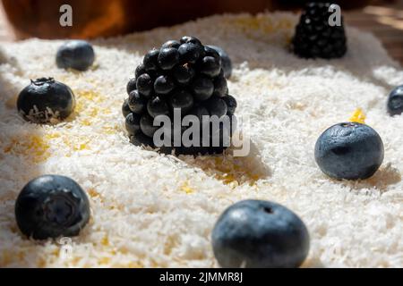 Close-up of a delicious homemade carrot cake decorated with grated coconut, blackberries and blueberries, suitable for vegetarians and vegans. Stock Photo