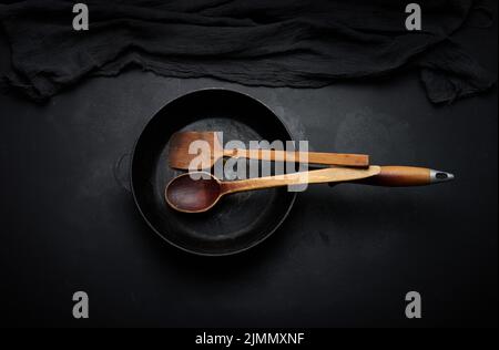 Empty round cast iron frying pan with wooden handle on black table, top view Stock Photo