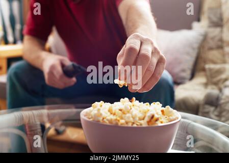 Caucasian man sitting on sofa with popcorn and tv remote Stock Photo