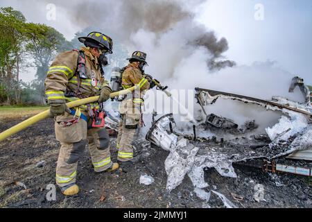 A two-man hose team wearing breathing apparatus hoses down the remains of a trailer fire as members of the Amagansett Fiire Department held a live-fir Stock Photo