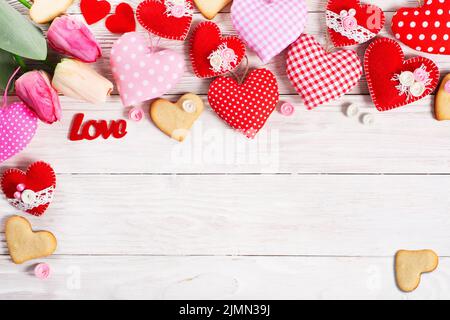 Handmade sewed Valentine fabric hearts with tulips and cookies flat lay background on white wooden table Stock Photo