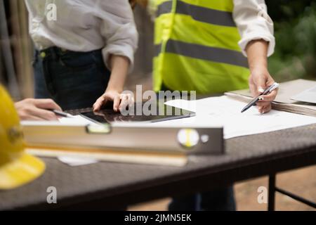 architector and engineers with draft plan of building and tablet computer talking on constructing site. Stock Photo