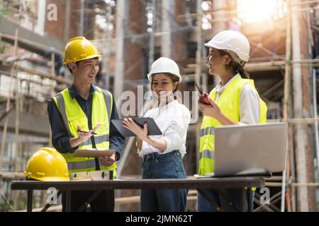 architector and engineers with draft plan of building and tablet computer talking on constructing site. Stock Photo