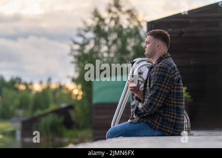 Profile portrait of a young man sitting in a wooden jetty drinking coffee and watching the sunset Stock Photo