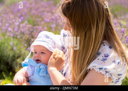 Caring young mother adjusting the sunhat on her baby outdoors on a summer day in a field of lavender Stock Photo