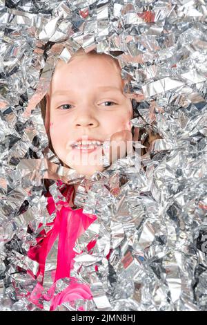Smiling cheerful face of a girl in a huge pile of confetti made of silver foil, close-up. A girl in sparkling sequins. Happy birthday, Christmas, New Stock Photo