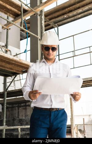 Man architect or businessman wearing hard hat and holding blueprints on a construction site Stock Photo