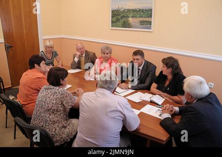 Middle aged men and women teachers sitting at the table in the office and communicating. Typical meeting in the teacher's room of the Ukrainian second Stock Photo