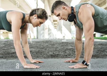 Athletic couple and fitness training outdoors. Man and woman doing push-ups exercise. Stock Photo