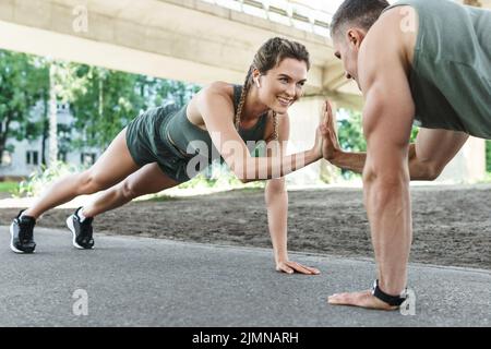 Athletic couple and fitness training outdoors. Man and woman doing push-ups exercise. Stock Photo