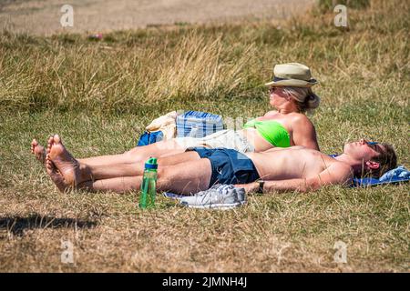 Wimbledon, London, UK. 7 August 2022  A couple sunbathing  in the warm sunshine on a parched grass on Wimbledon Common as the hot weather and a lack of rainfall continue to grip much of the south of England and the UK, with temperatures expected to reach  above 30celsius  by next week Credit. amer ghazzal/Alamy Live News Stock Photo