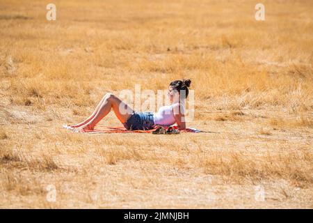 Wimbledon, London, UK. 7 August 2022  A woman sunbathing  on the parched grass on Wimbledon Common  on another  hot day  as the UK's heatwave and drought continues into August, with temperatures expected to reach  above 30celsius  by next week Credit. amer ghazzal/Alamy Live News Stock Photo