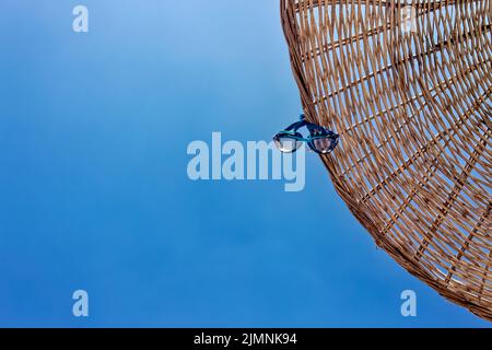 Swim goggles hanging on a parasol umbrella. View from directly below with copy space. Clear, sunny, open sky. Stock Photo