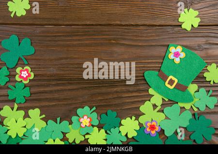 Happy Saint Patrick's mockup of handmade felt hat flowers and shamrock clover leaves on wooden background. Stock Photo