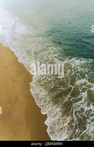 High angle view of large wave washing over a sandy beach Stock Photo