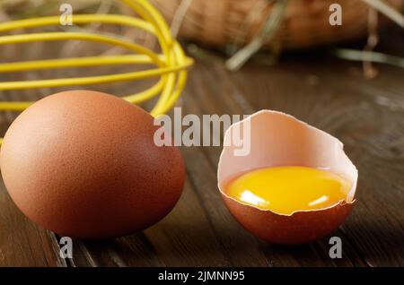 Raw organic brown chicken broken eggs with yolk wicker basket and whisk on kitchen wooden table Stock Photo